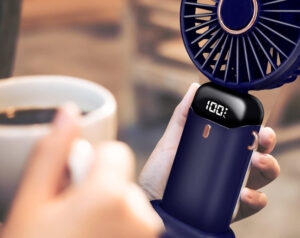 Personne en terrasse prenant un café tout en se ventilant avec un mini ventilateur portable
